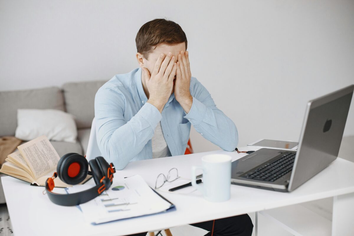 Adult man sitting at a desk with his head in his hands, showing signs of stress and difficulty focusing, which is a common experience for adults living with ADHD